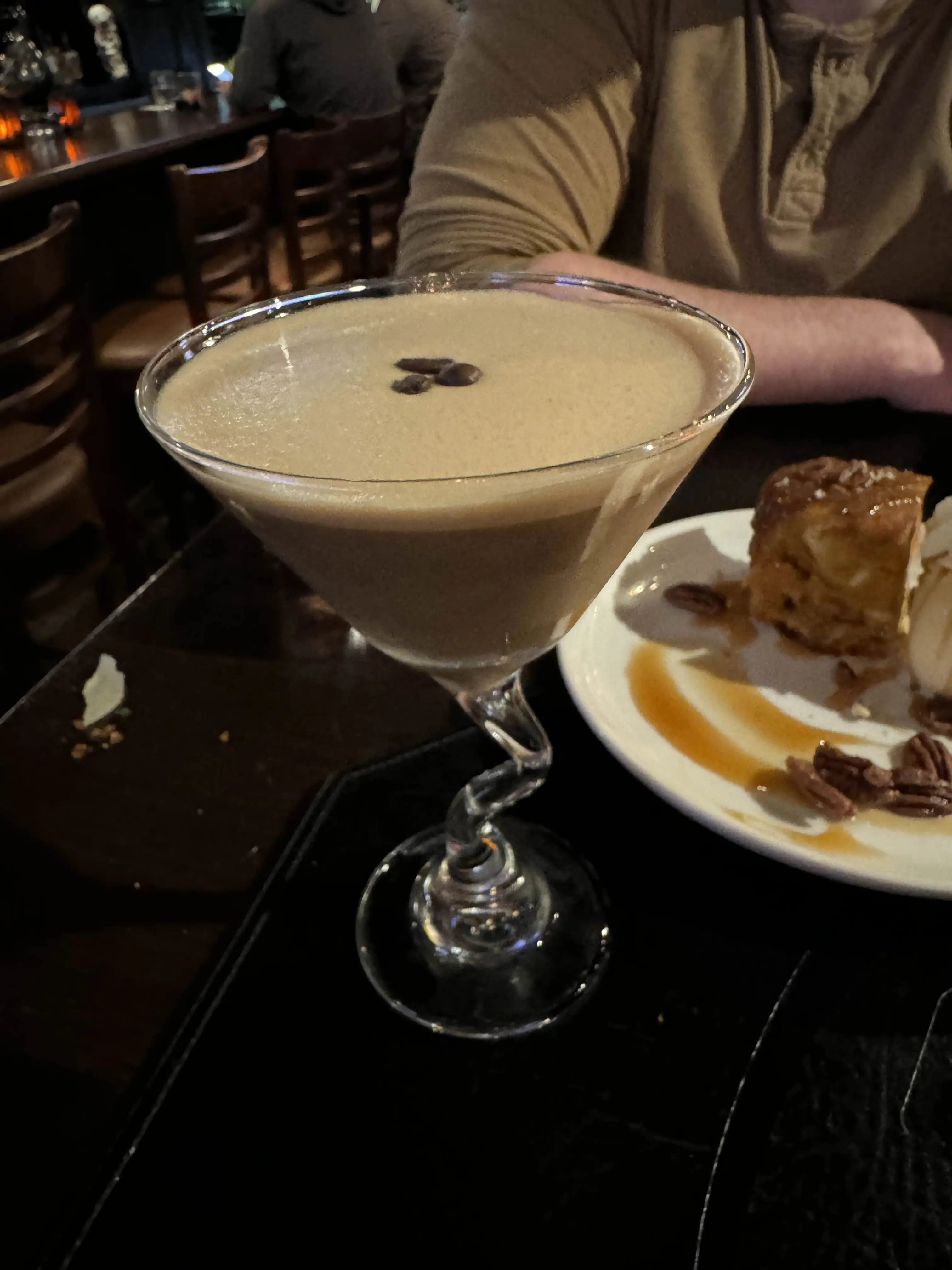A martini glass of espresso martini, foamy on top with three espresso beans floating in a row, on a dark table.
