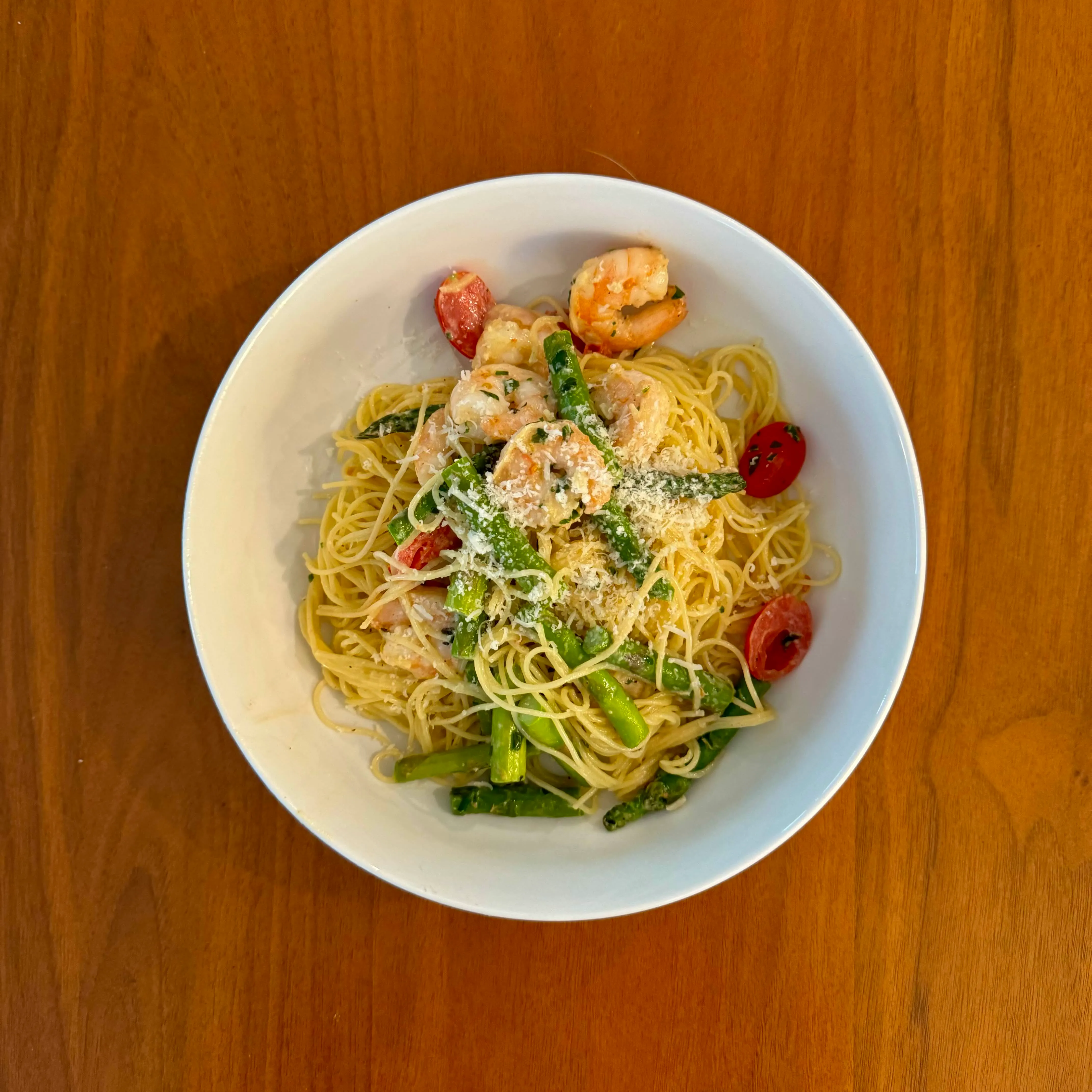 A bowl of angel-hair pasta tossed with shrimp, green asparagus tips, cherry tomatoes, and a dusting of parmesan.
