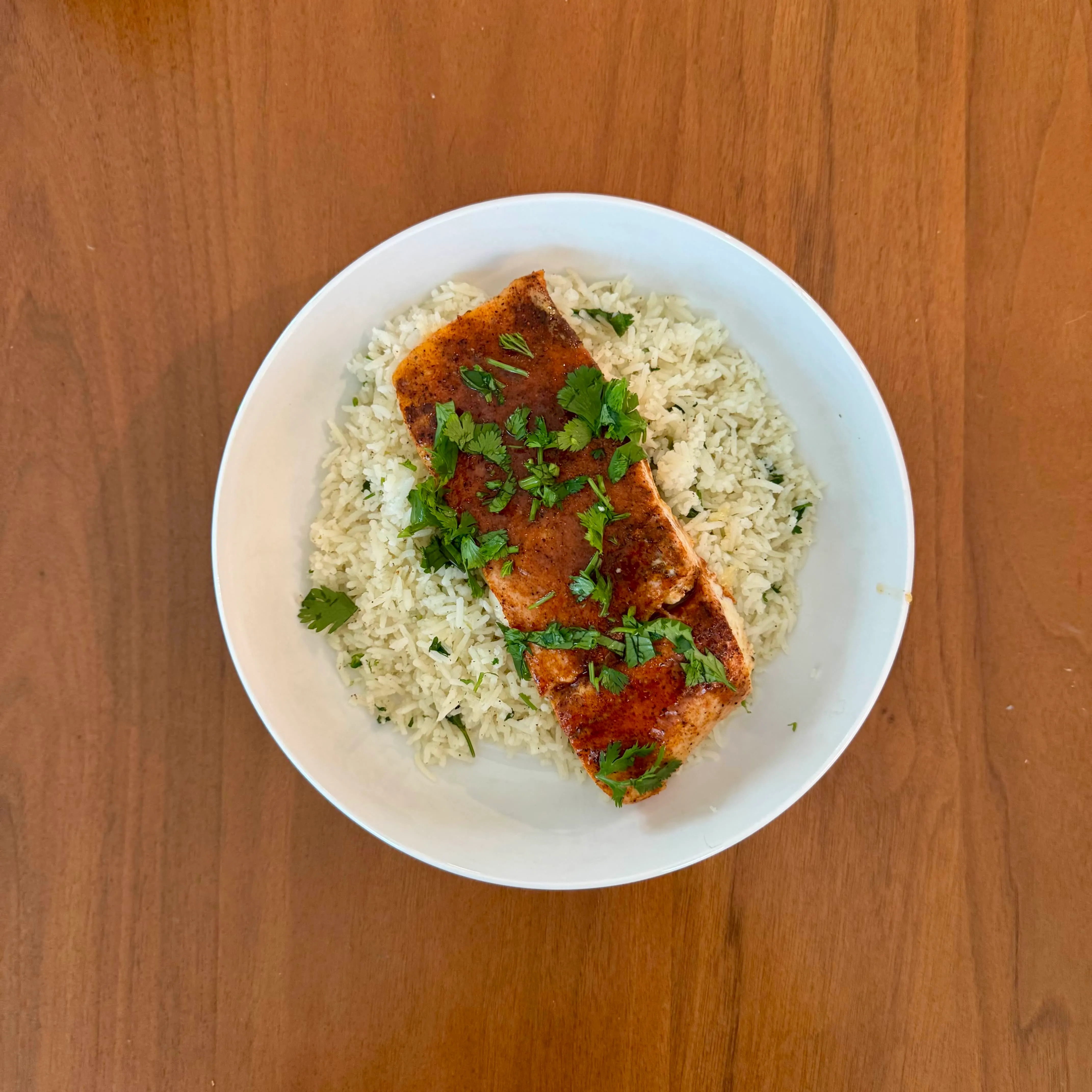 A bowl of pale cilantro-lime rice with a single blackened salmon fillet laid across it and a scatter of torn cilantro.