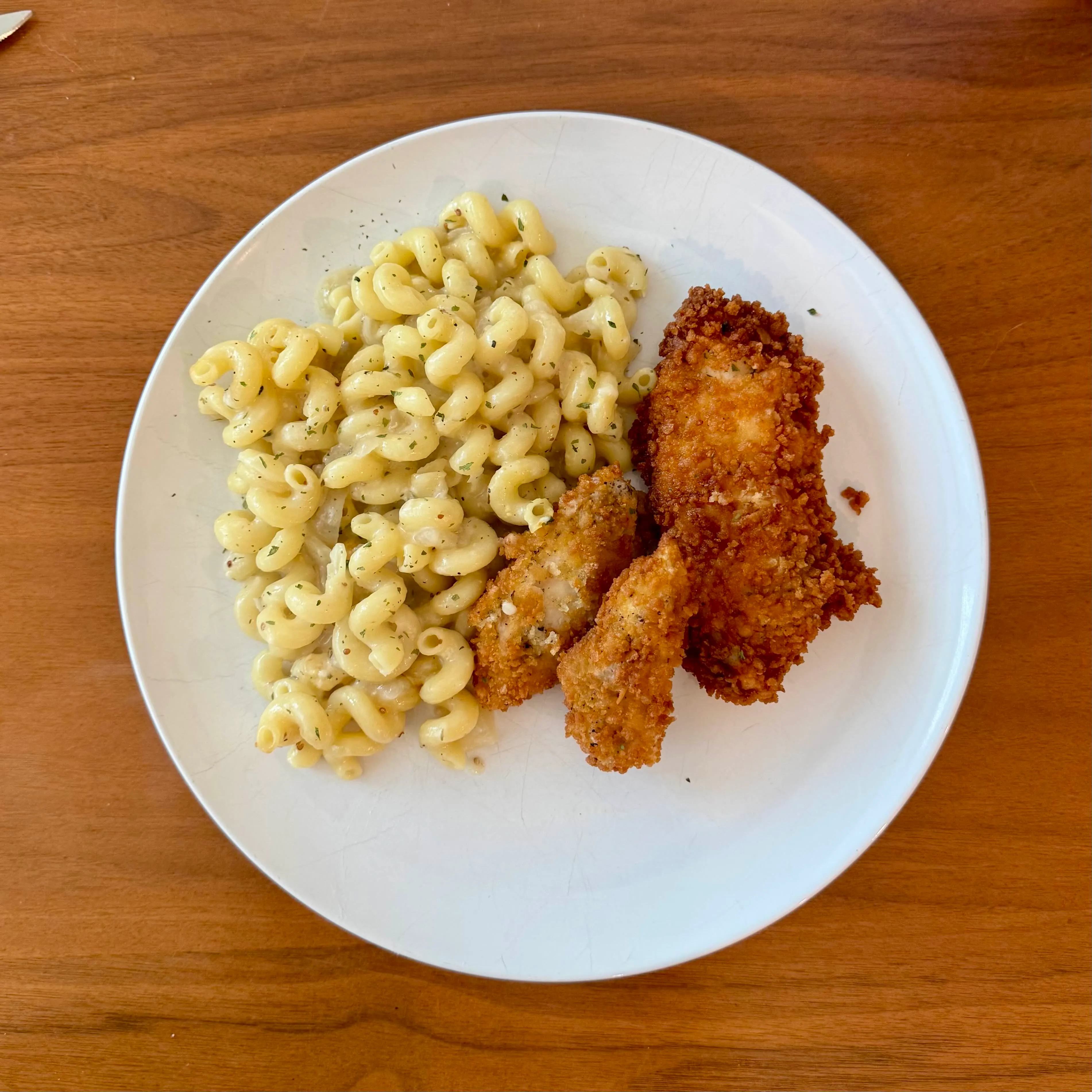 A plate with a mound of creamy cavatappi mac and cheese beside three thick crispy fried chicken tenders.