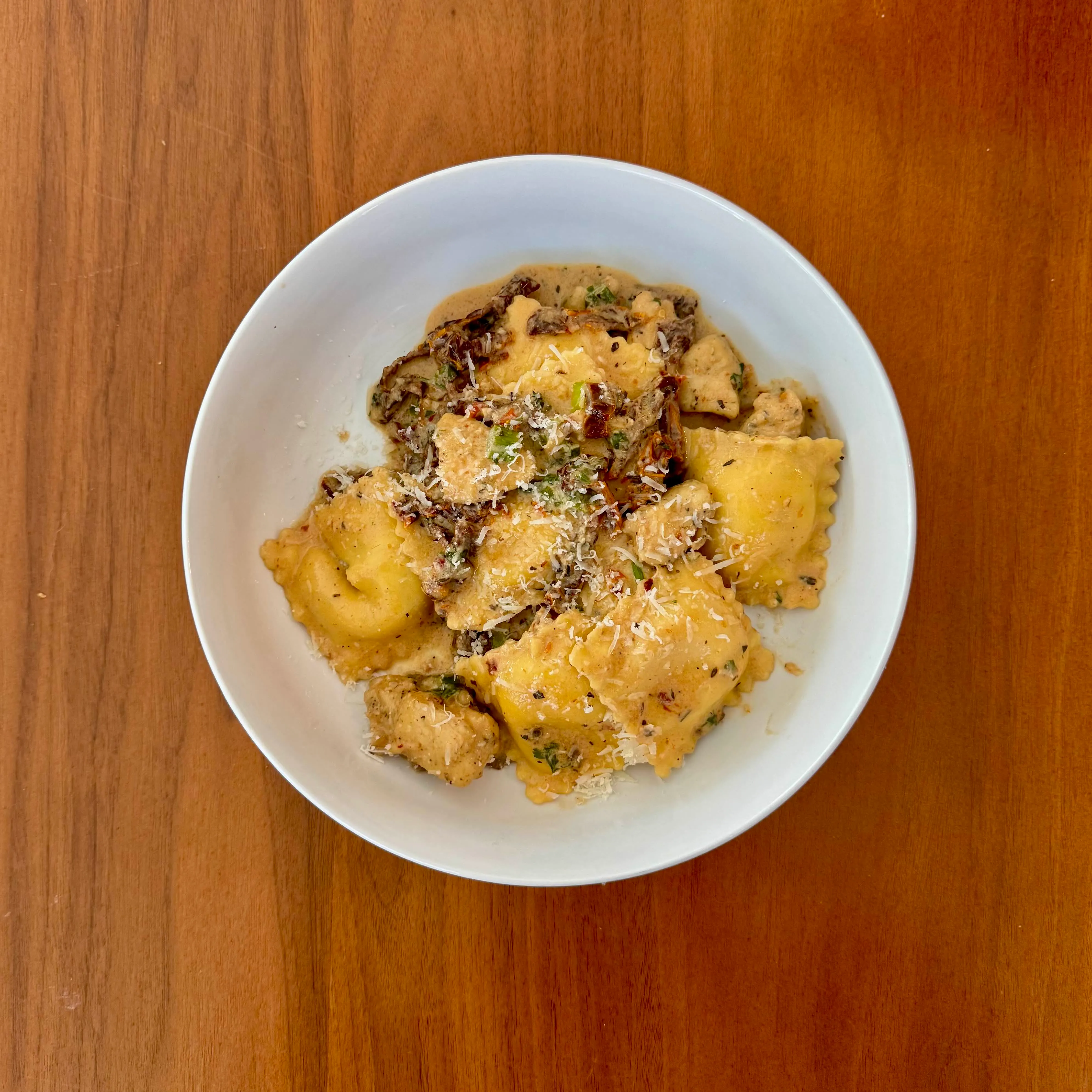 A bowl of cheese ravioli mixed with chicken pieces and sliced mushrooms in a creamy parmesan-herb sauce.