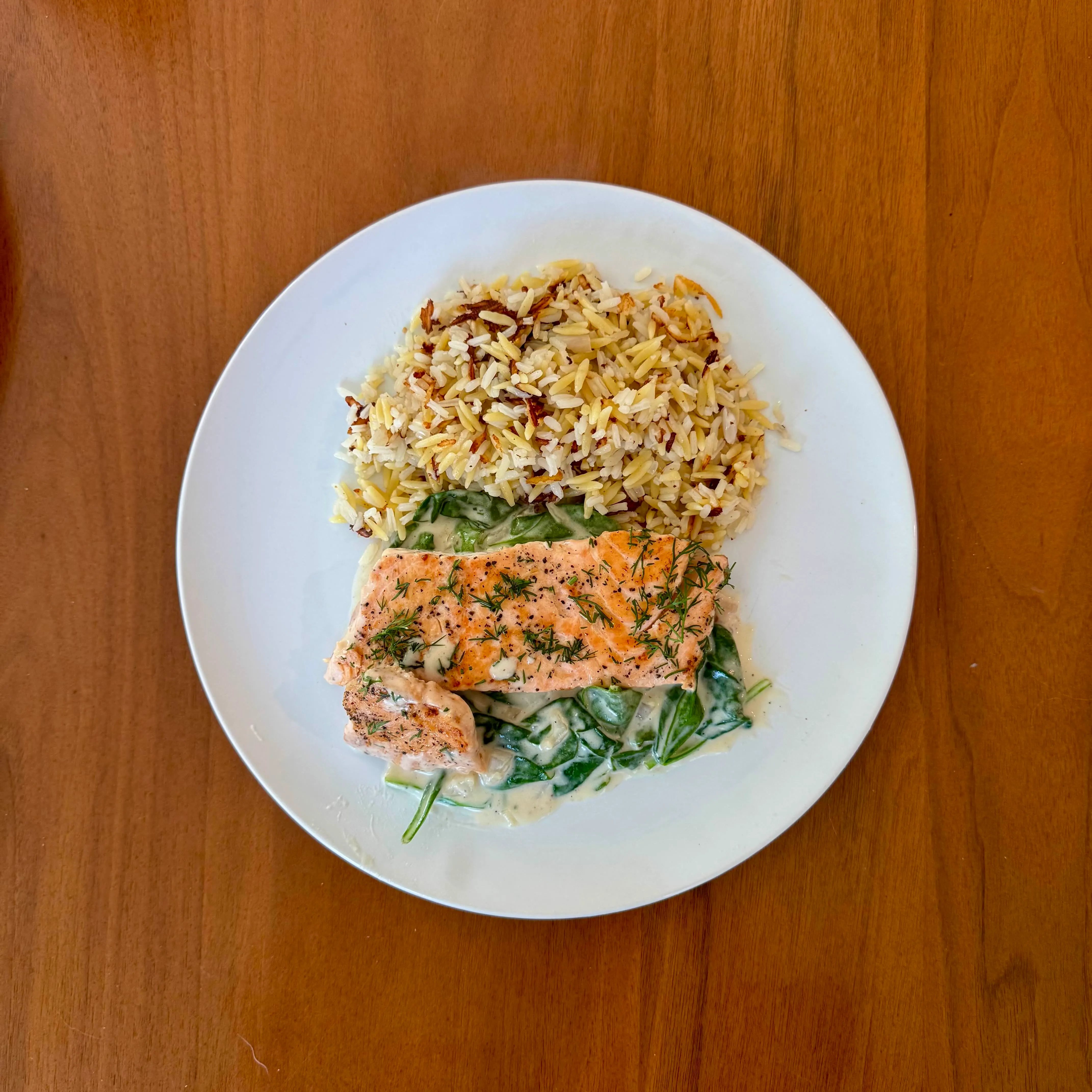 A pink salmon fillet with dill resting on a pool of creamed spinach, beside a mound of brown-and-white wild rice blend.
