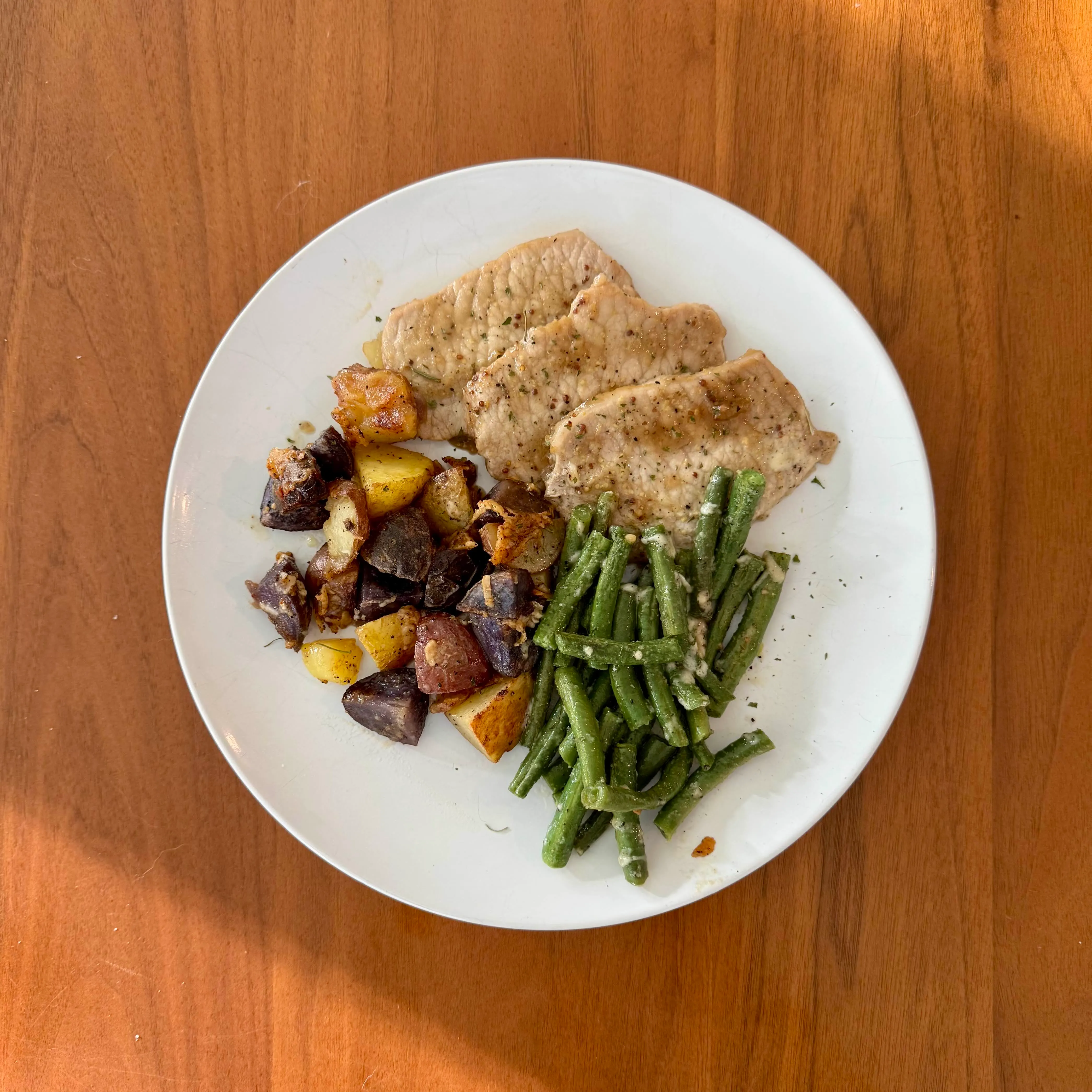 Thin pan-fried pork chops with a pile of roasted potatoes - golden, deep-purple, and red - alongside garlicky green beans.