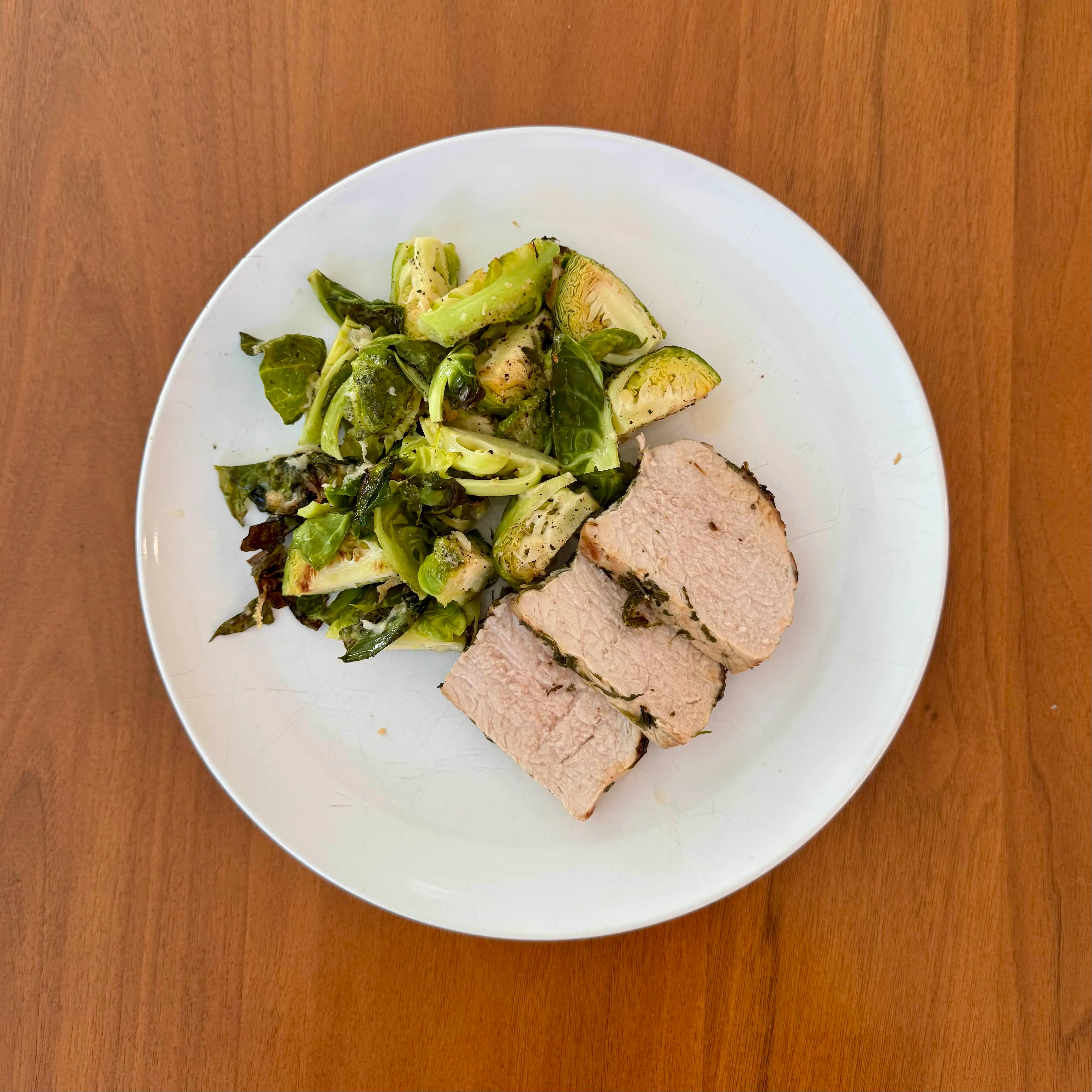 Sliced pork tenderloin with a blackened crust beside a tangle of charred halved brussels sprouts and torn kale.