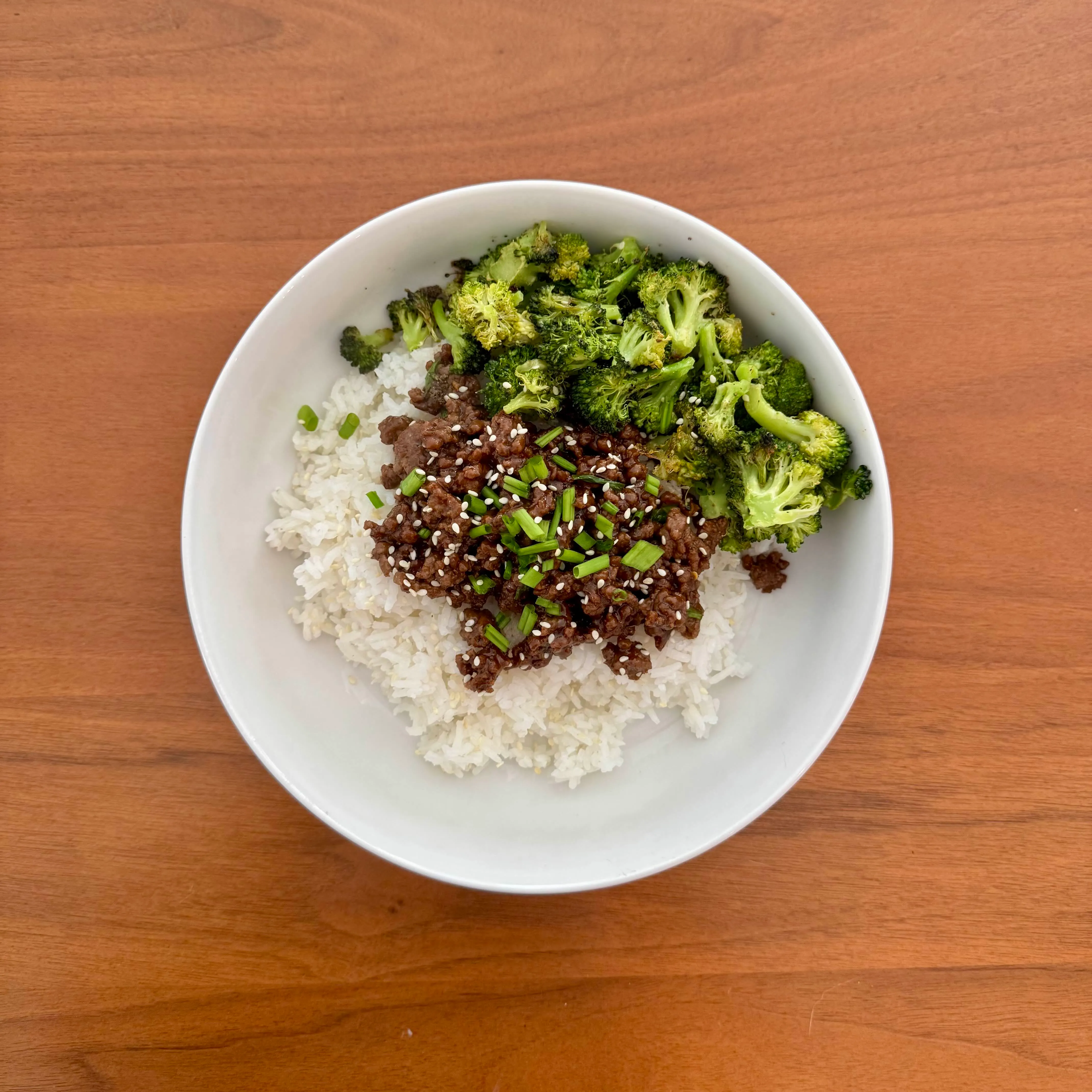A bowl of white rice with crumbled glossy bulgogi-style beef and a generous mound of charred broccoli florets, dusted with sesame seeds and green onion.