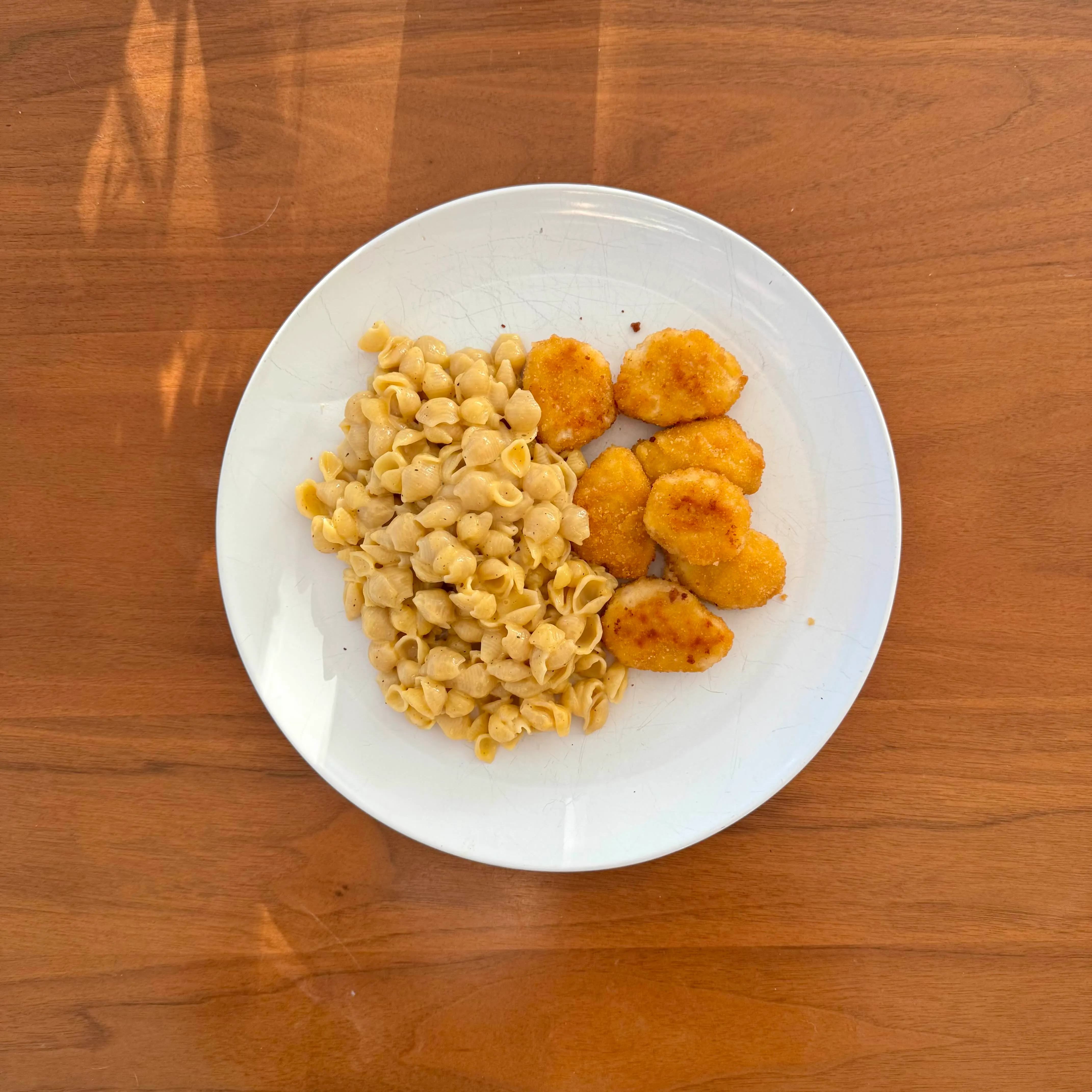 A plate of white-cheddar shell pasta beside a few round breaded chicken nuggets.