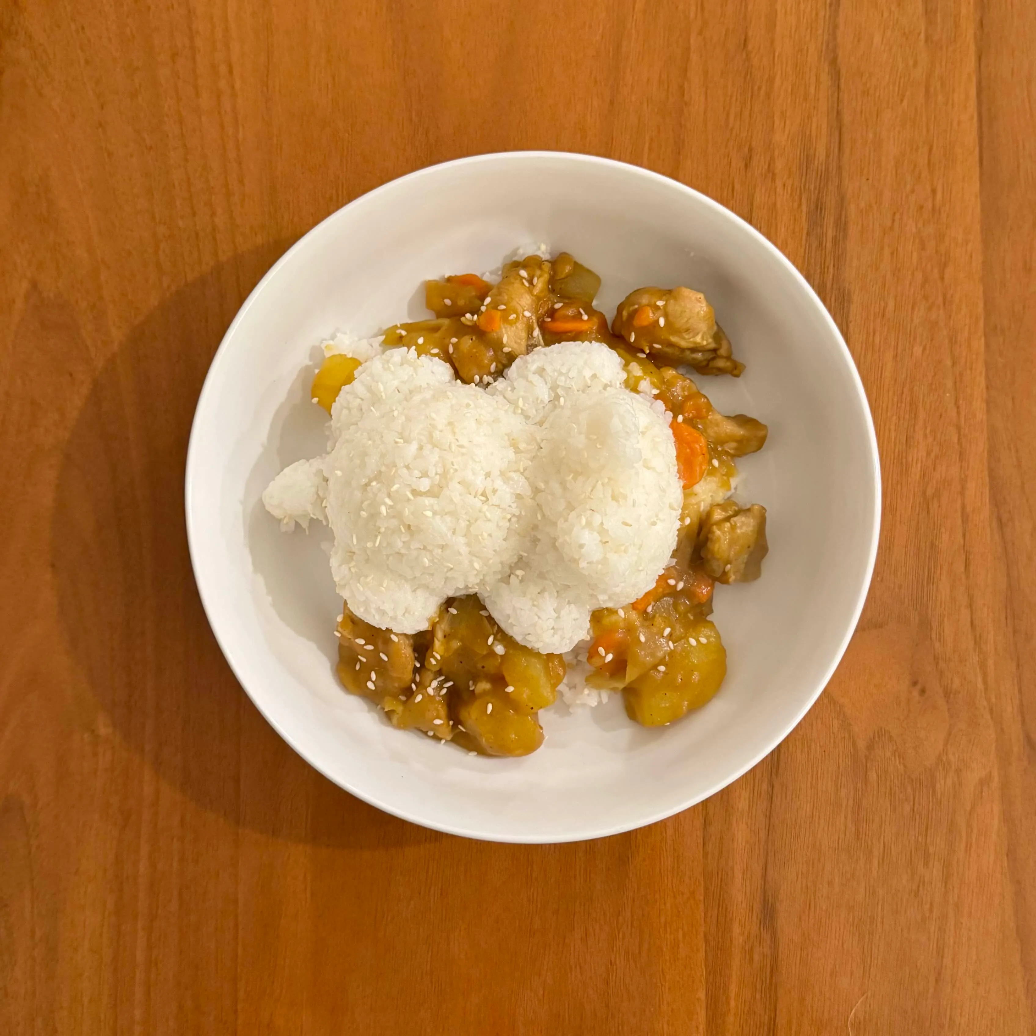A bowl of white rice scooped over sweet-and-sour chicken with pineapple, carrot, and sesame seeds.