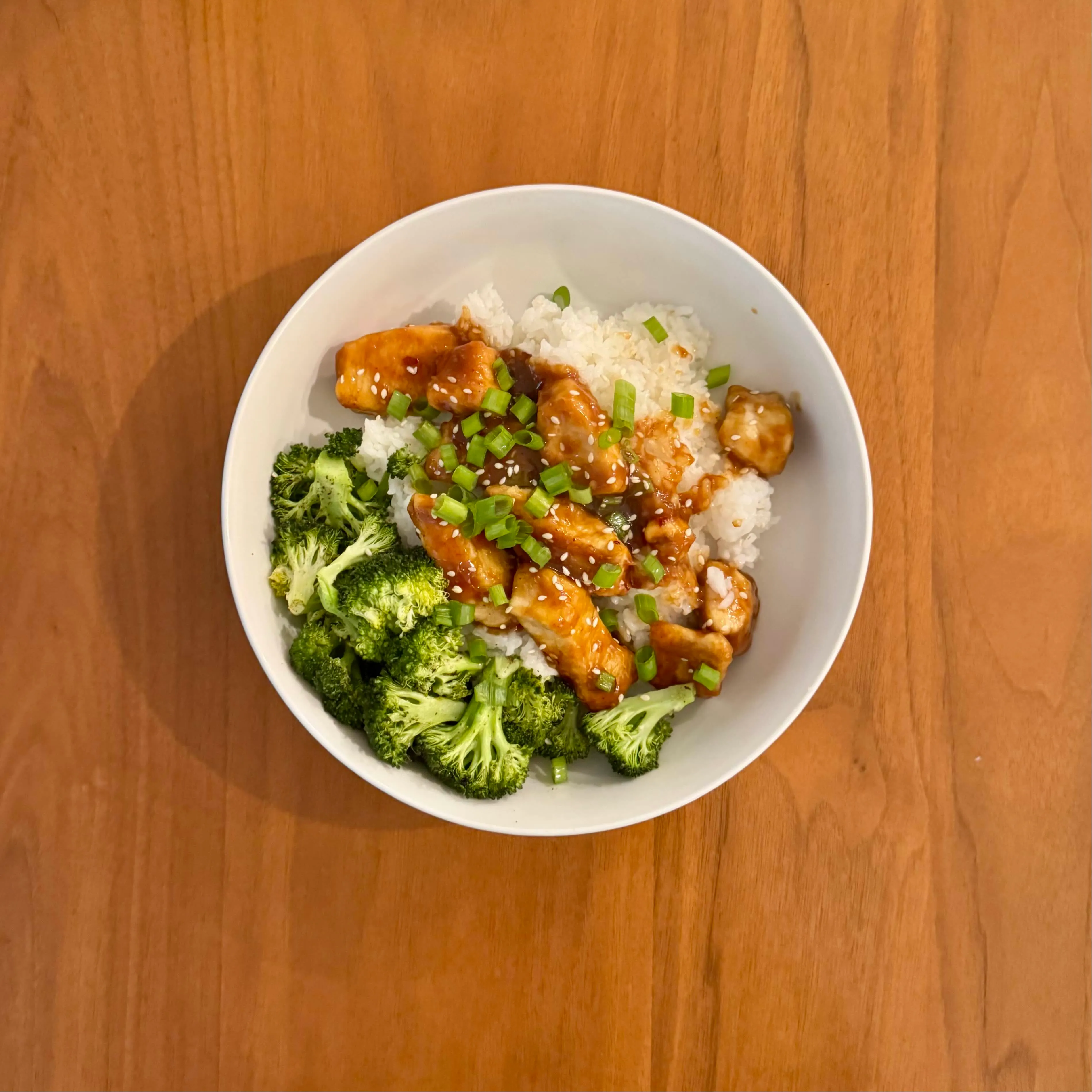 A bowl of teriyaki chicken over white rice with bright-green roasted broccoli and sliced scallions.