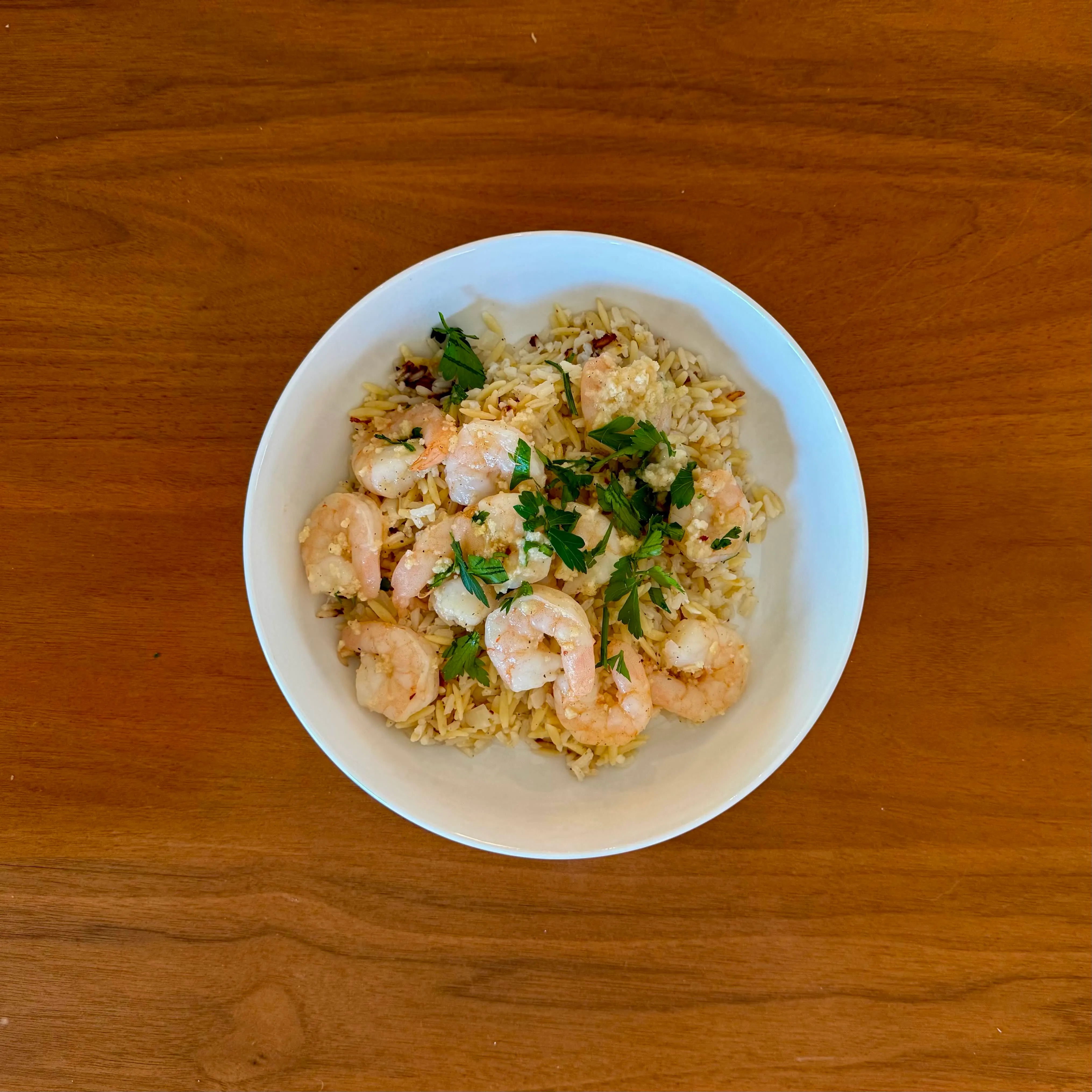 A shallow bowl of pink shrimp with orzo, crumbled feta, and torn parsley.