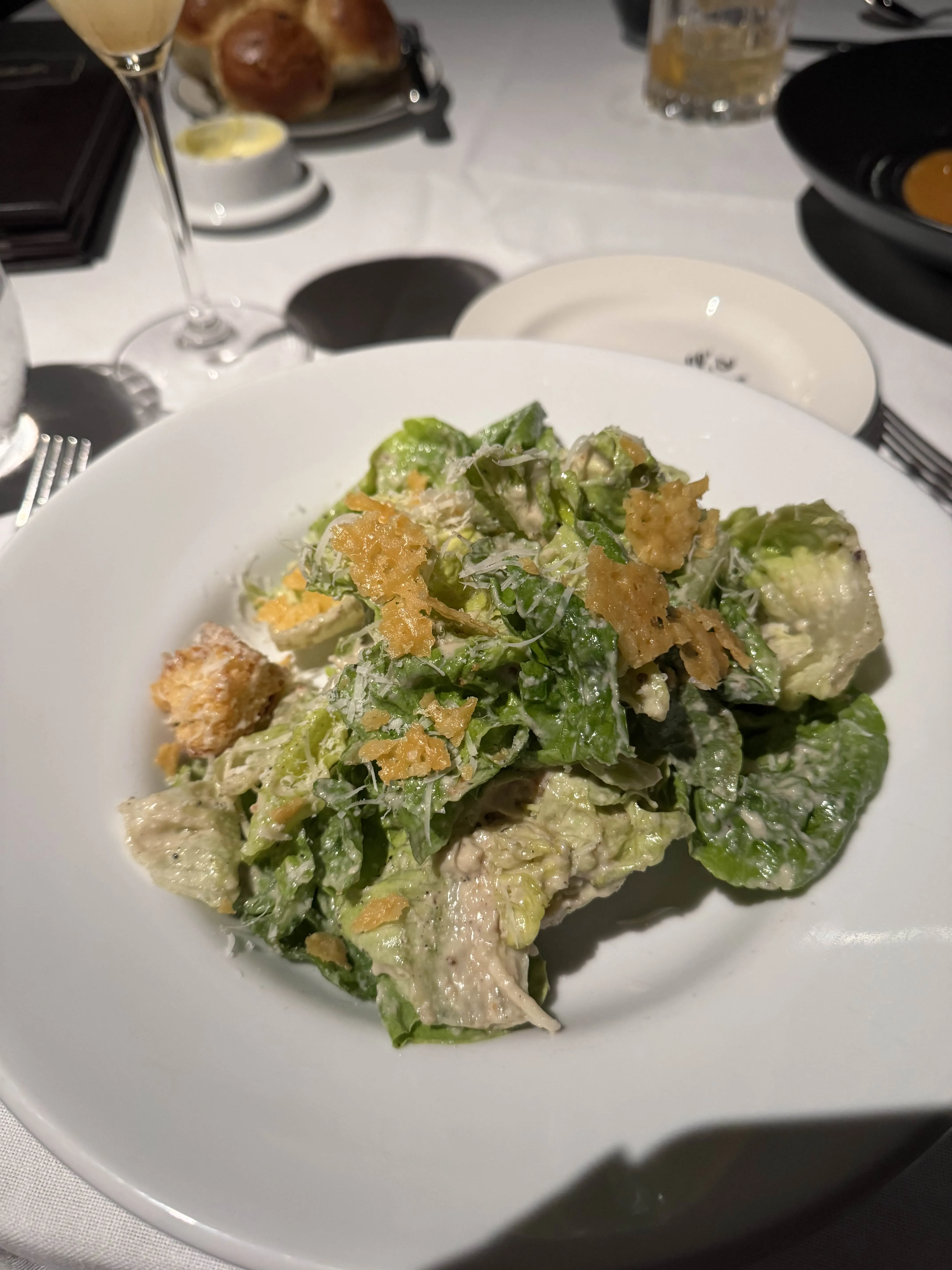 A shallow white bowl of caesar salad - torn romaine, shaved parmesan, and frico crisps.