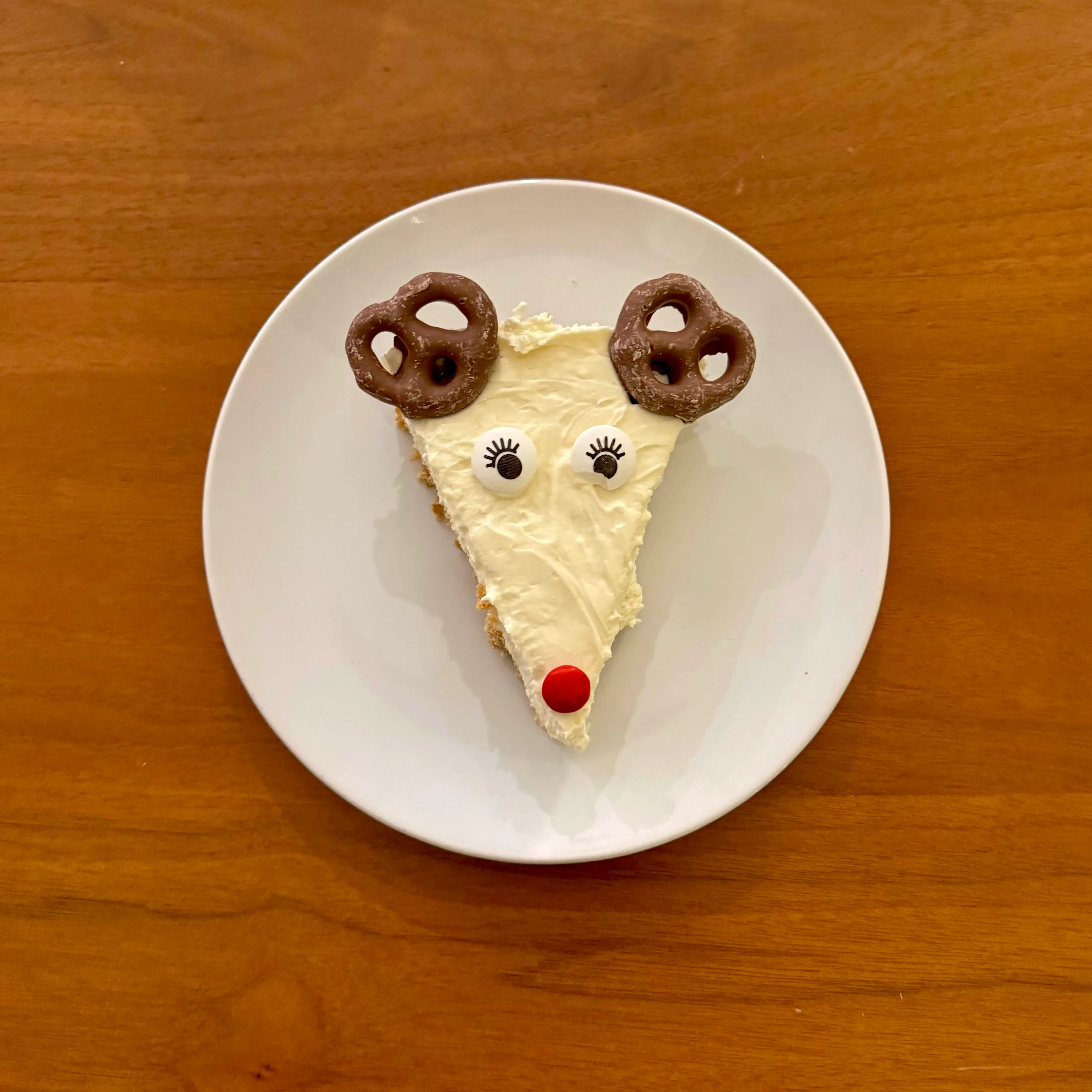 A wedge of white-chocolate cheesecake decorated to look like a reindeer - two chocolate-covered pretzels for antlers, two candy eyes, and a red M&M for a nose.